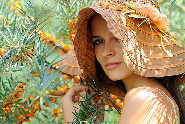 Ragazza in un cappello vicino ad un cespuglio dell'olivello spinoso